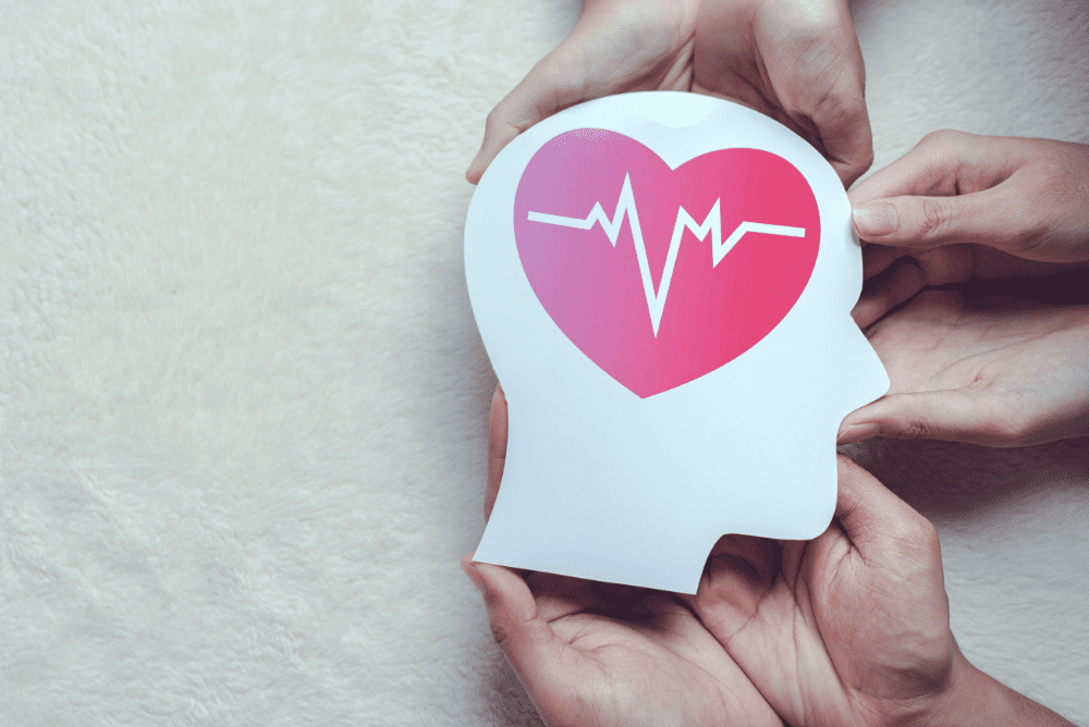 Hands holding a paper cutout of a head with a heart and heartbeat