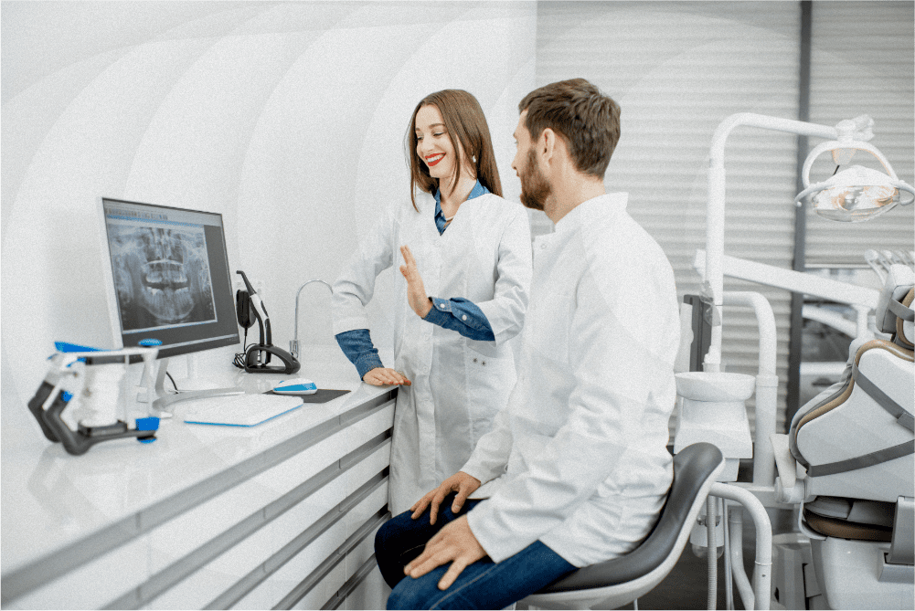 Two dental professionals in white coats review dental X-rays on a computer screen in a modern clinic.