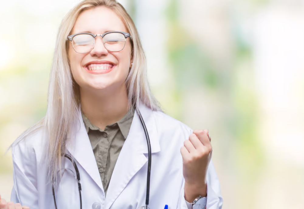 A woman in a lab coat smiles confidently, showcasing her professionalism and enthusiasm in a laboratory setting.