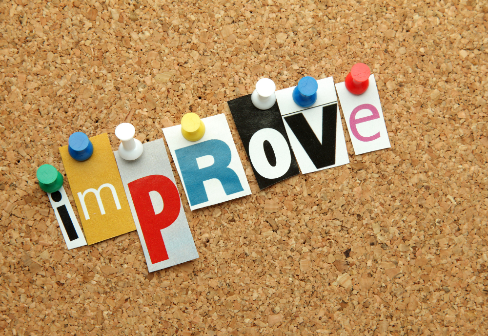 Colorful cut-out letters spelling "improve" displayed on a cork board background.